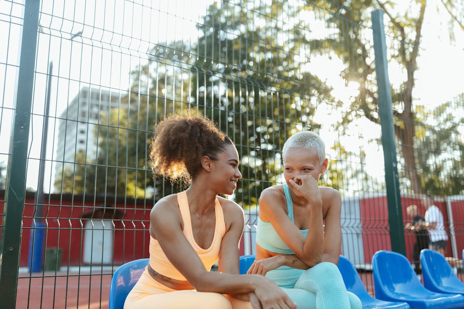 Two women in activewear sharing a moment of laughter outdoors on a sunny day.