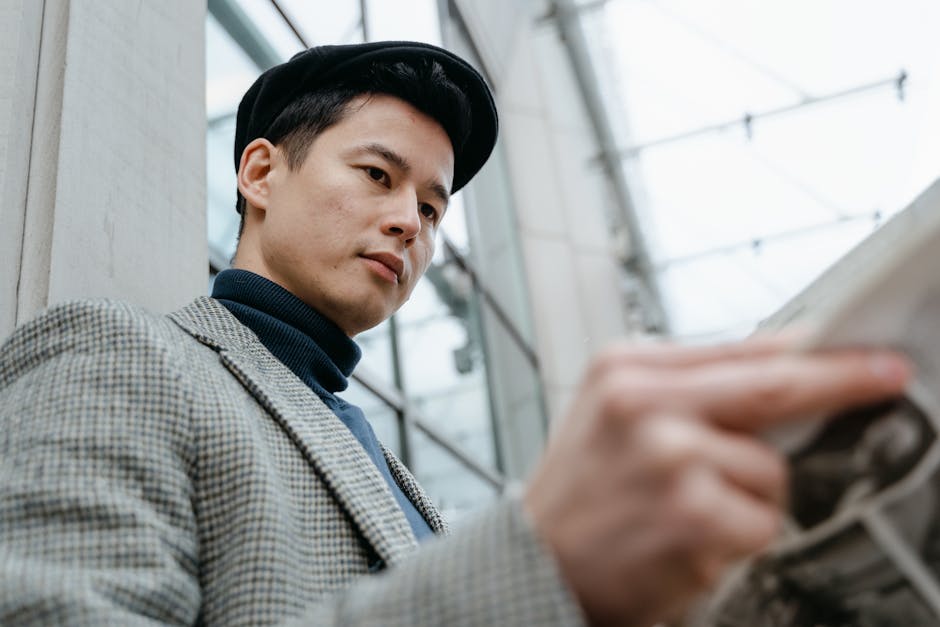 Low angle shot of stylish Asian man in gray suit holding newspaper outside urban building.