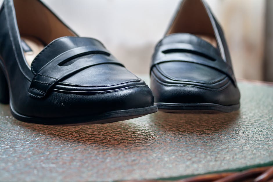 Close-up of stylish black leather women's shoes on a textured glass table.