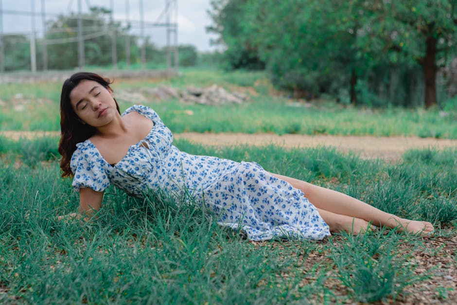 A serene portrait of an Asian woman in a blue floral dress relaxing in a green park.