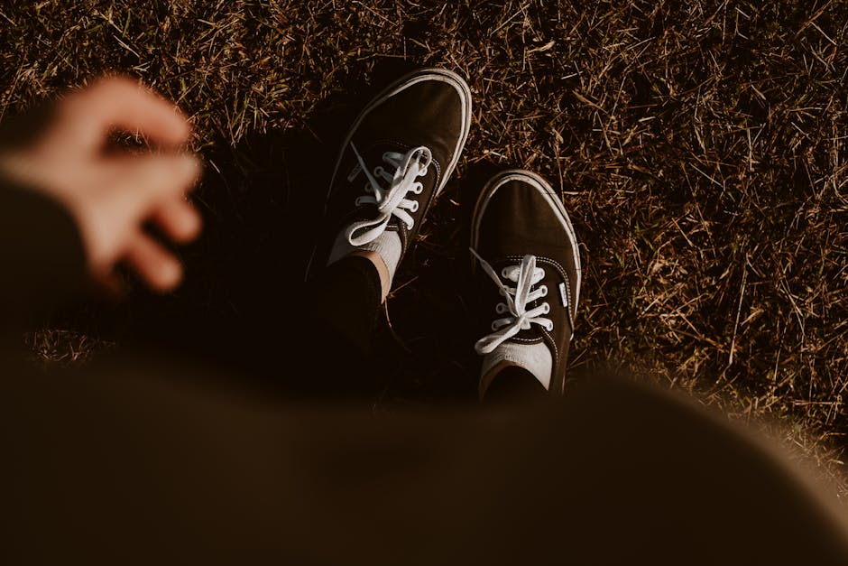 A pair of black sneakers on dry grass at daytime, capturing a casual, outdoor fashion vibe.